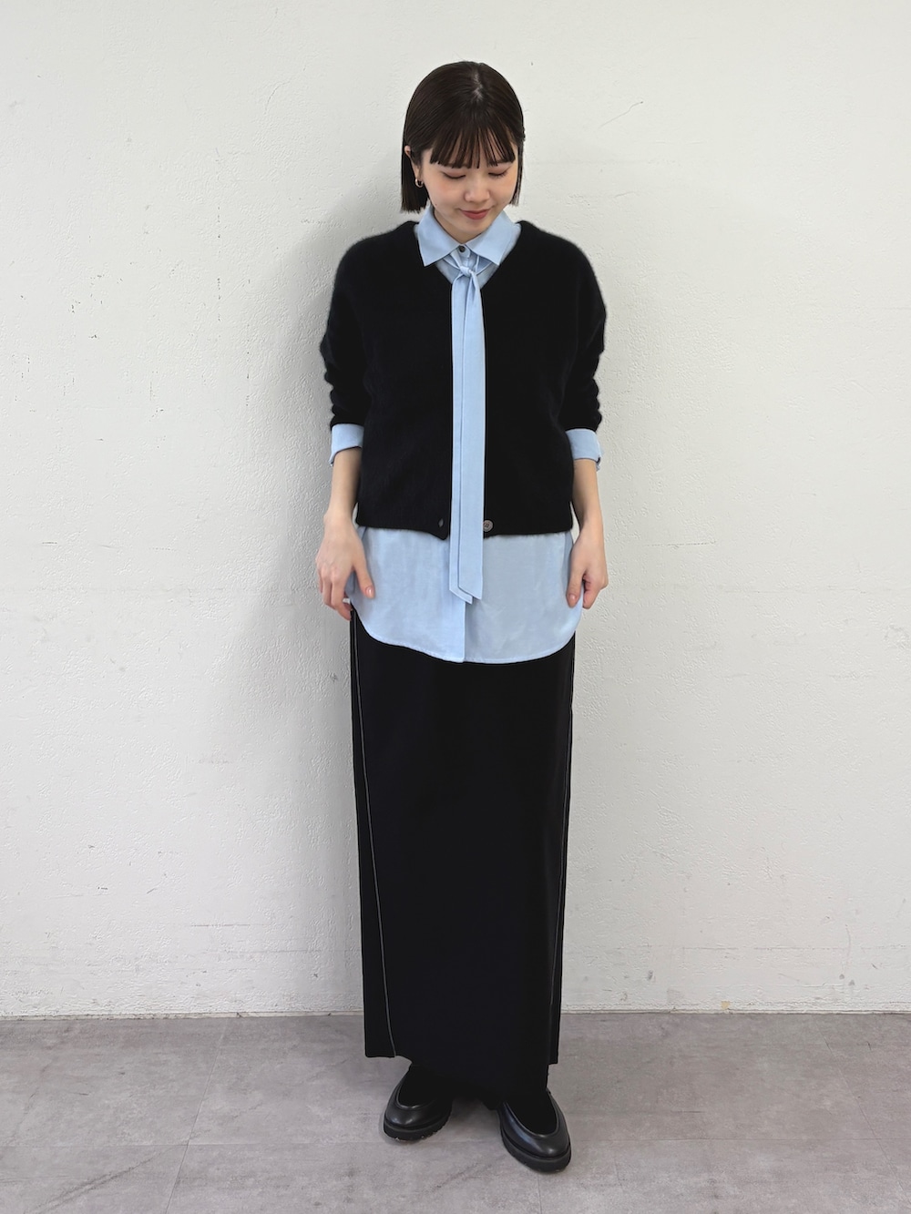 ブラック系のカーディガン/ボレロ、ブルー系のシャツ/ブラウス、ブラック系のスカートを着用したレディースの秋コーディネートの2枚目の写真