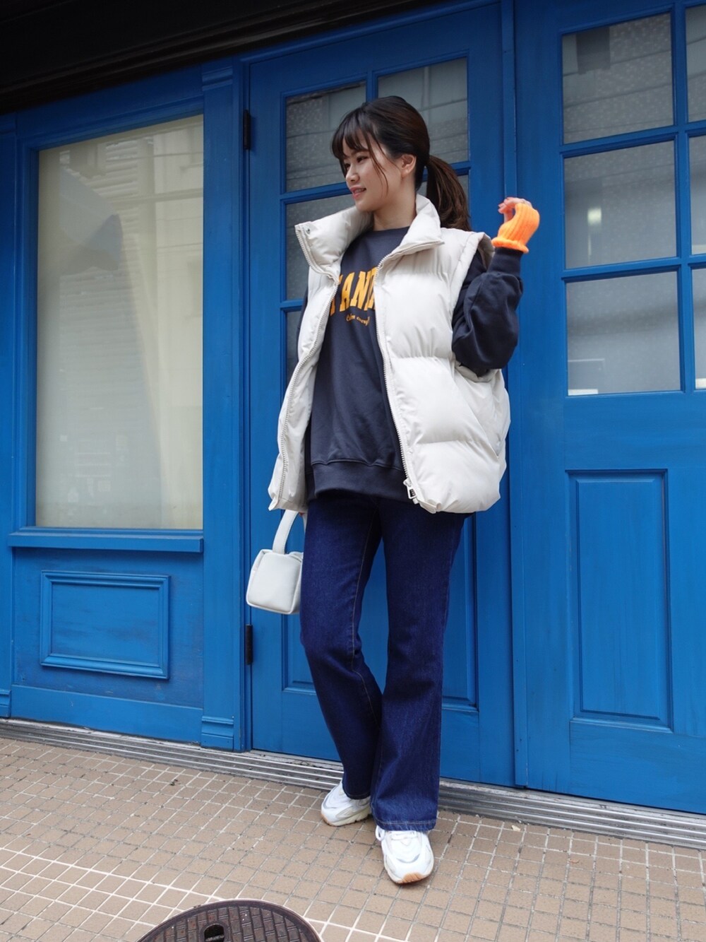 ブルー系のスウェット、ベージュ系のダウンベスト、ホワイト系のショルダーバッグを着用したレディースの秋コーディネートの2枚目の写真