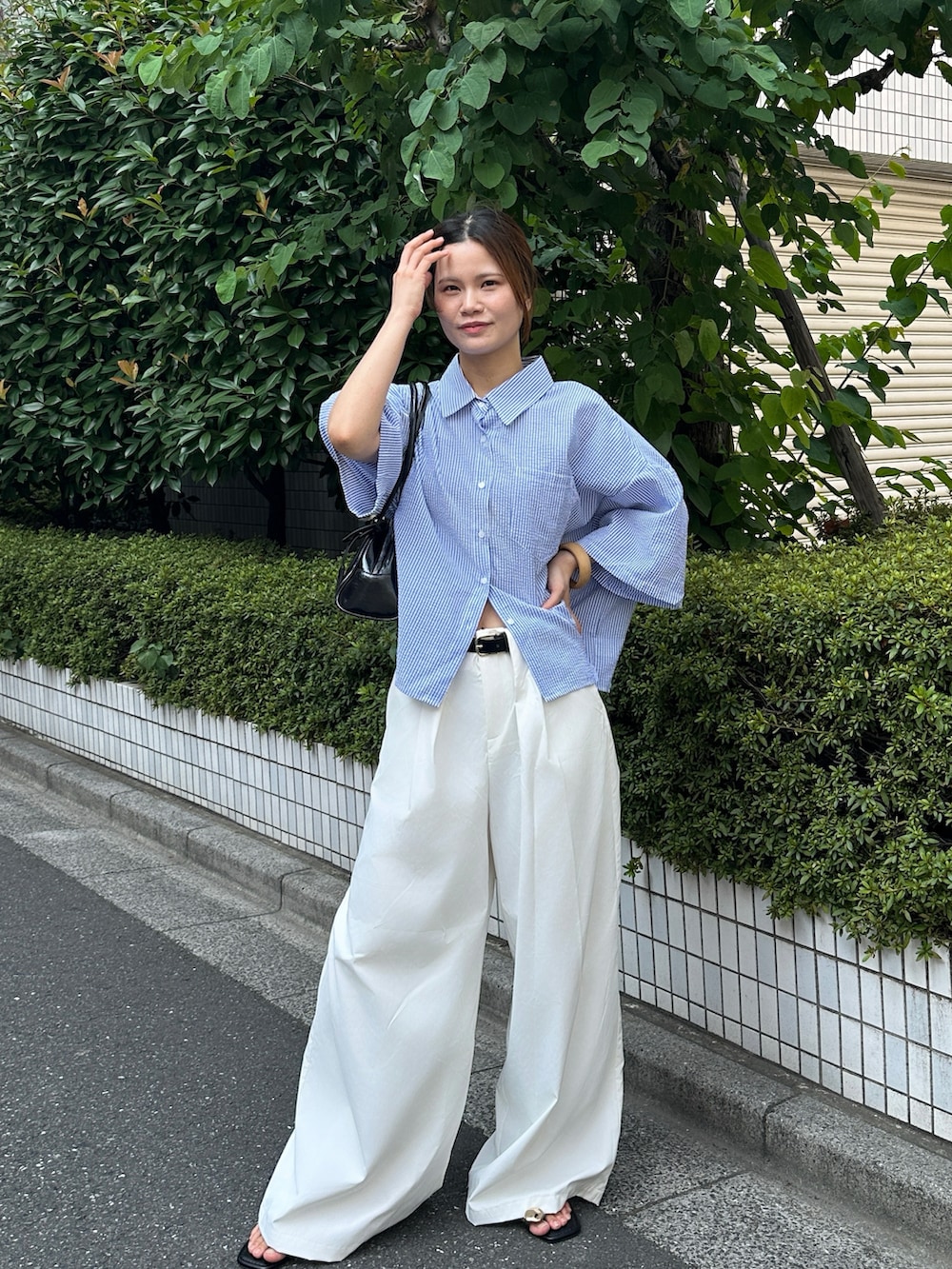 ホワイト系のスラックス、ブルー系のシャツ/ブラウス、ブラック系のハンドバッグを着用したレディースの夏コーディネートの2枚目の写真