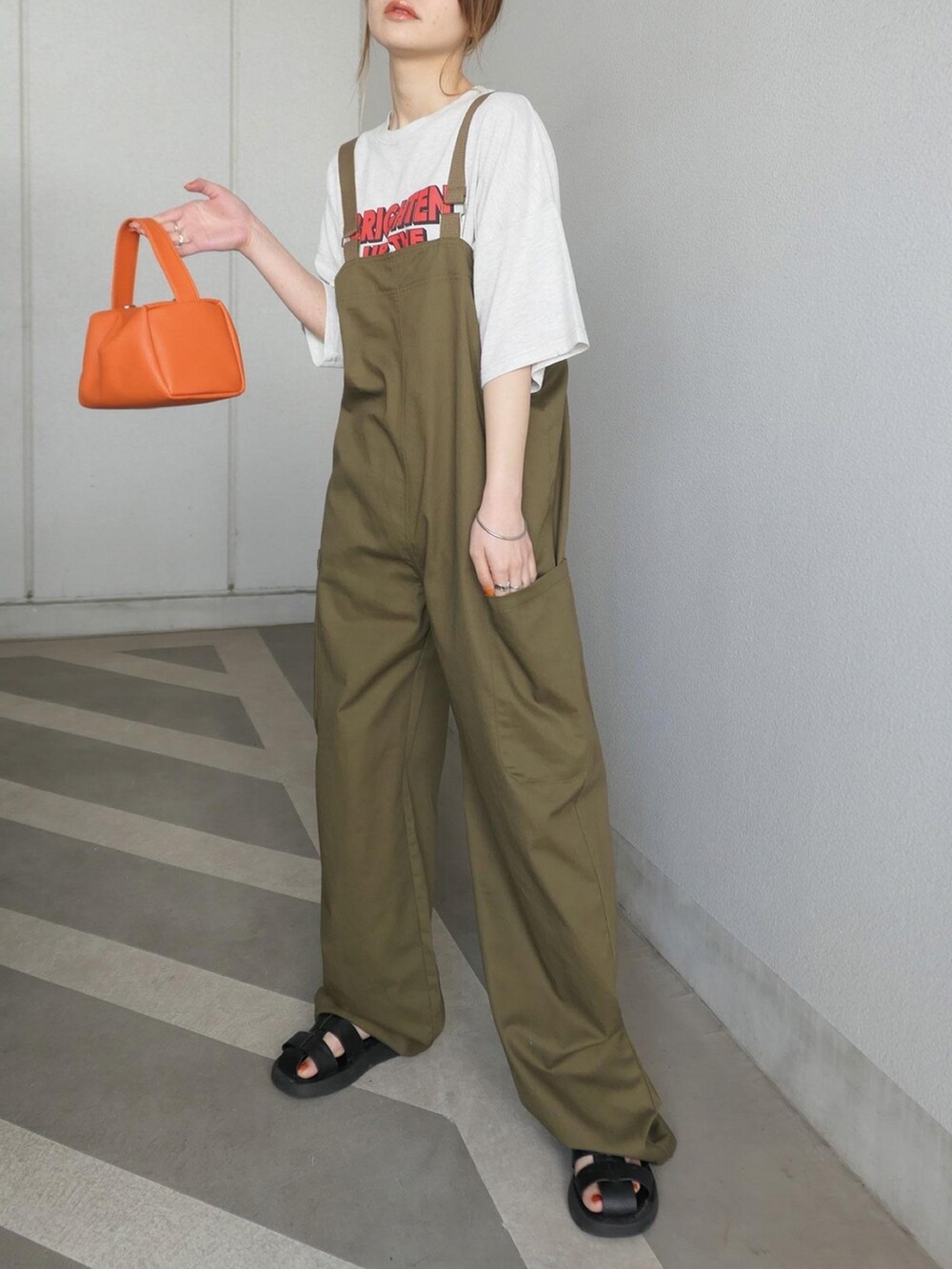 グリーン系のサロペット/オーバーオール、オレンジ系のショルダーバッグ、ベージュ系のTシャツ/カットソーを着用したレディースの春コーディネートの2枚目の写真