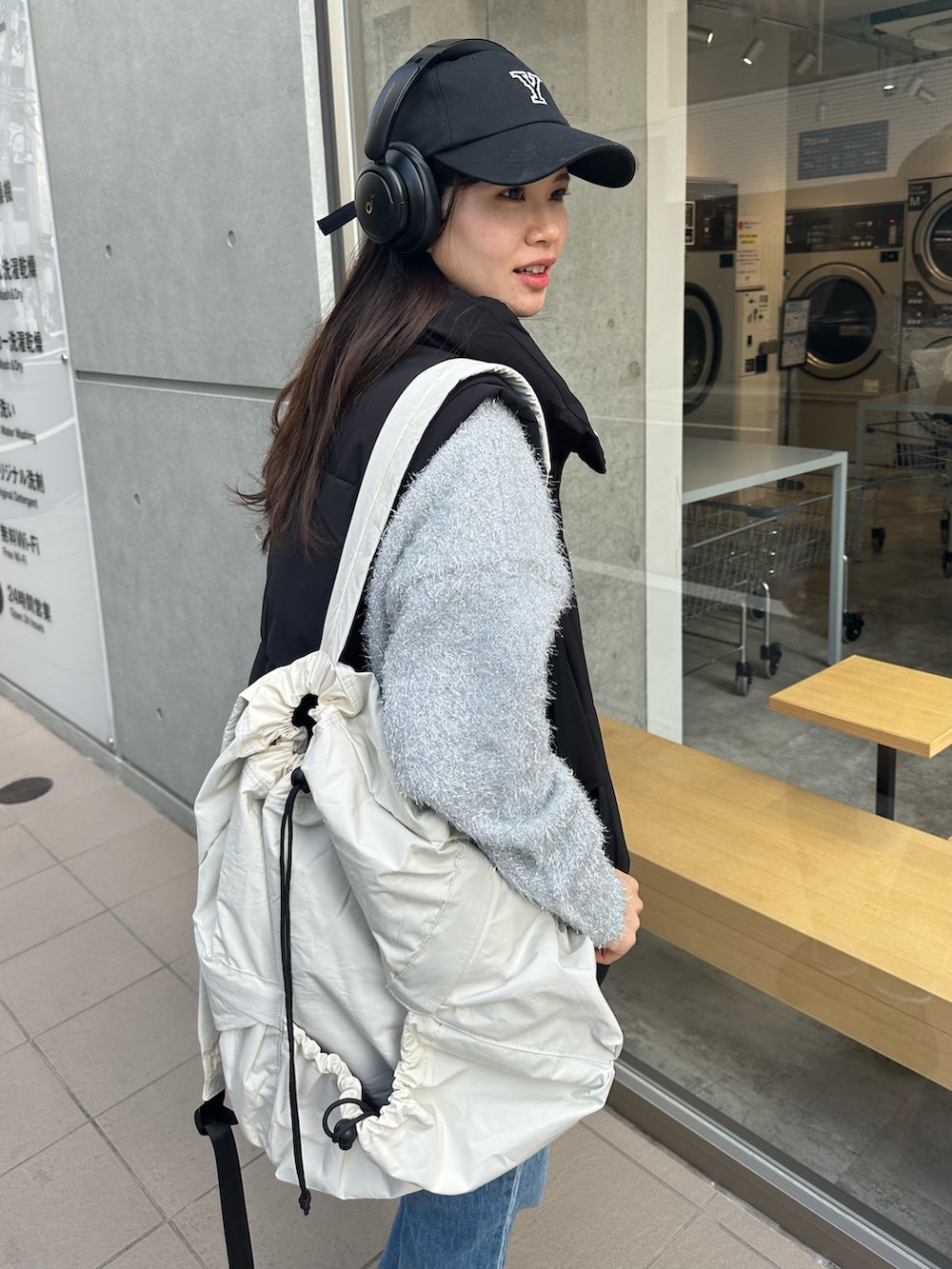 シルバー系のニット/セーター、ブラック系のダウンベスト、ホワイト系のバックパック/リュックを着用したレディースの冬コーディネートの2枚目の写真