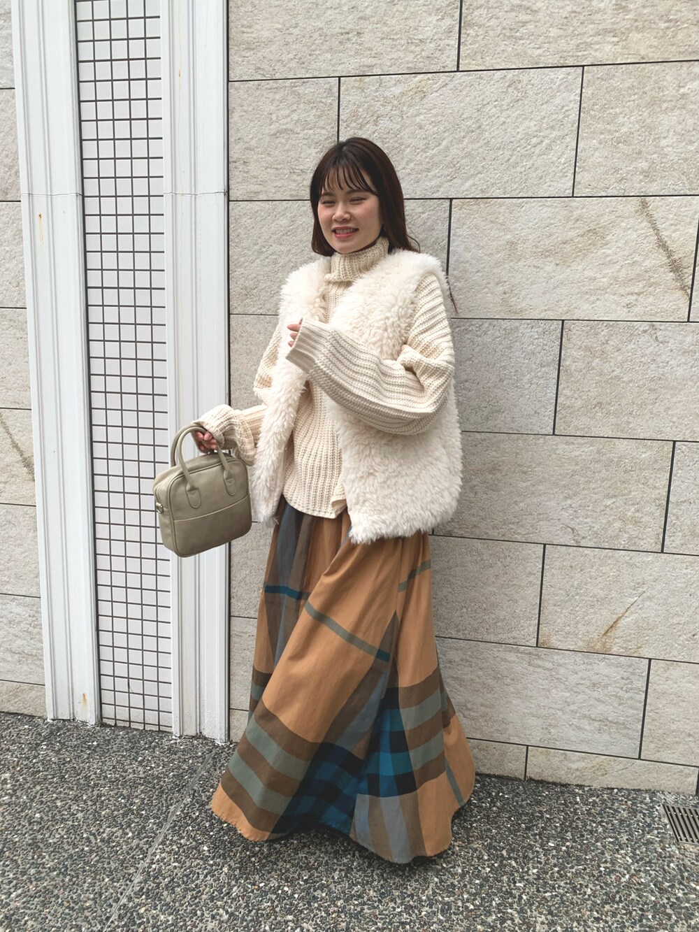 イエロー系のスカート、ベージュ系のショルダーバッグ、ホワイト系のニット/セーターを着用したレディースの冬コーディネートの2枚目の写真