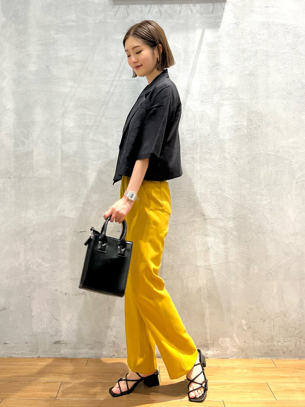 イエロー系のスラックス、ブラック系のサンダル、ブラック系のショルダーバッグを着用したレディースの夏コーディネートの2枚目の写真