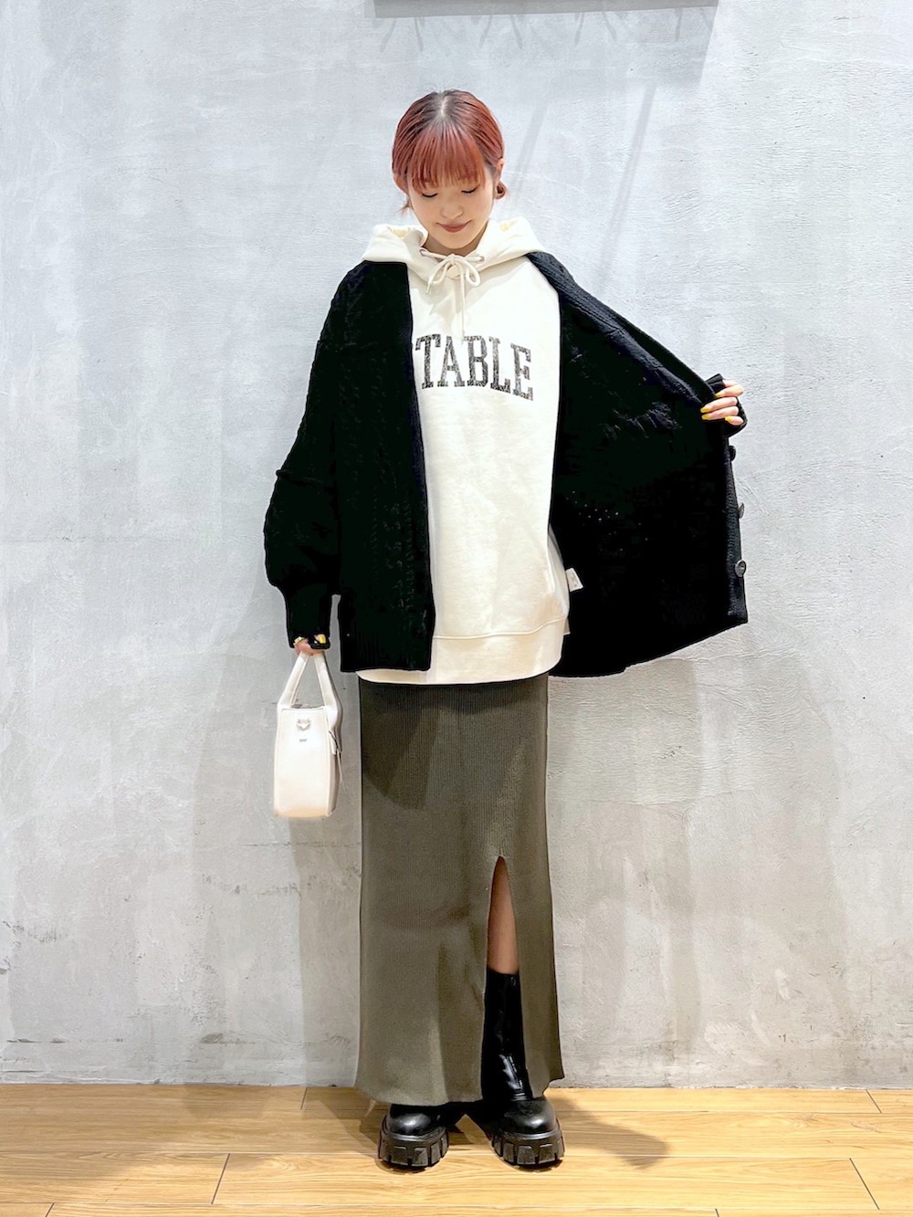 ホワイト系のパーカー、ブラック系のカーディガン/ボレロ、グリーン系のスカートを着用したレディースの秋コーディネートの2枚目の写真