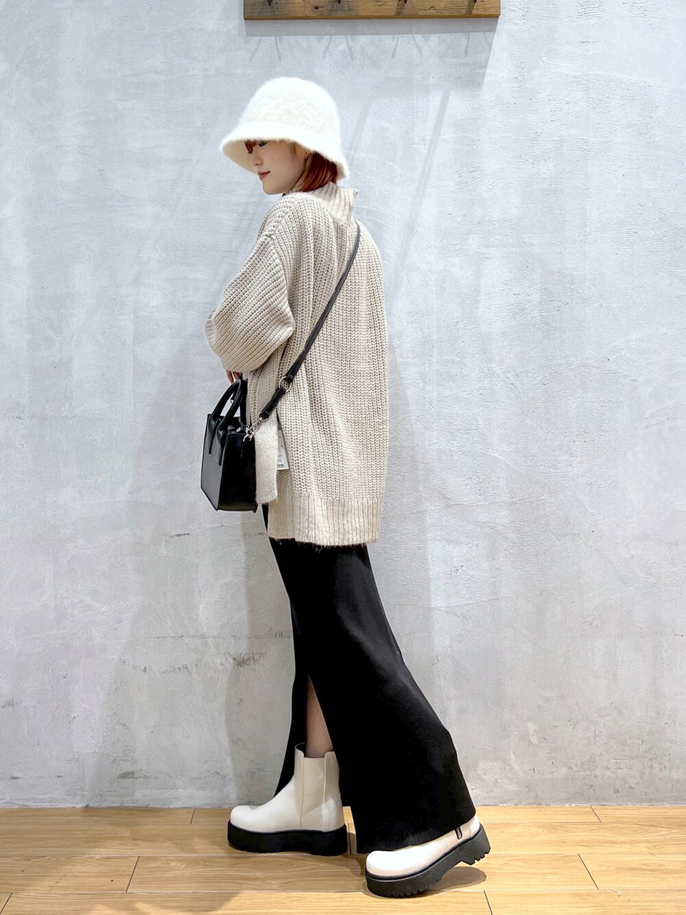 ブラック系のショルダーバッグ、ベージュ系のニット/セーター、ブラック系のスカートを着用したレディースの秋コーディネートの2枚目の写真