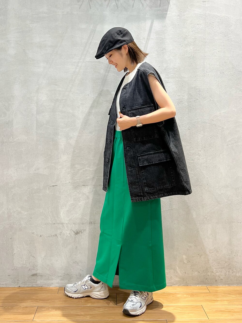 ブラック系のベスト、グリーン系のスカート、グレー系のスニーカーを着用したレディースの夏コーディネートの2枚目の写真