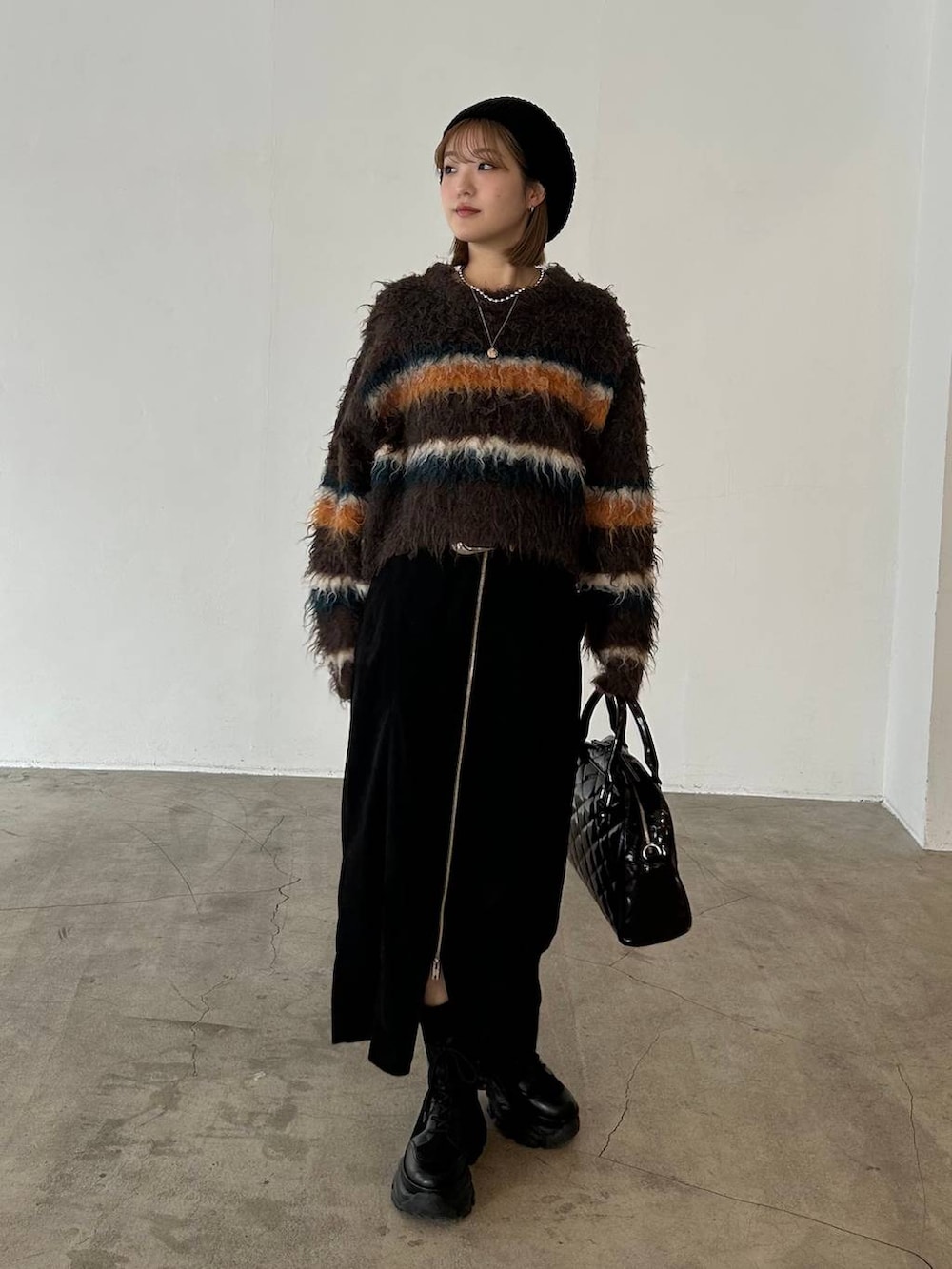 ブラック系のブーツ、ベージュ系のボストンバッグ、ブラウン系のニット/セーターを着用したレディースの冬コーディネートの2枚目の写真