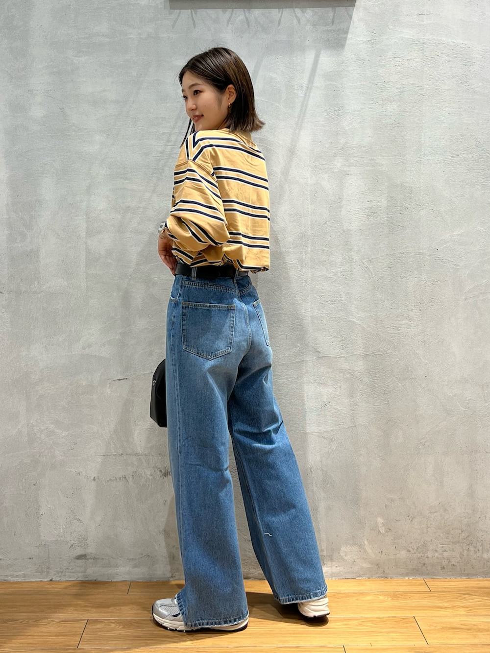 ブルー系のデニムパンツ、ブラック系のショルダーバッグ、グレー系のスニーカーを着用したレディースの秋コーディネートの2枚目の写真