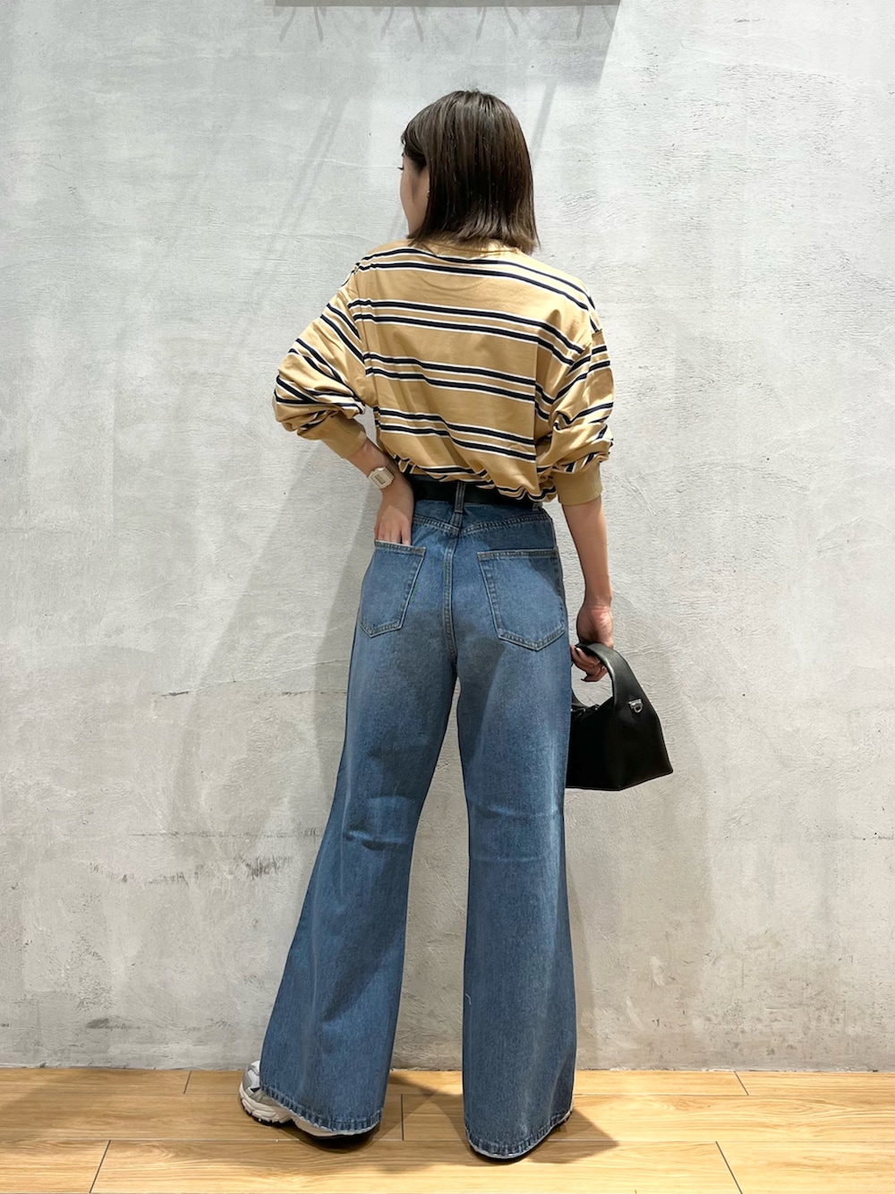 ブルー系のデニムパンツ、ブラック系のショルダーバッグ、グレー系のスニーカーを着用したレディースの秋コーディネートの3枚目の写真