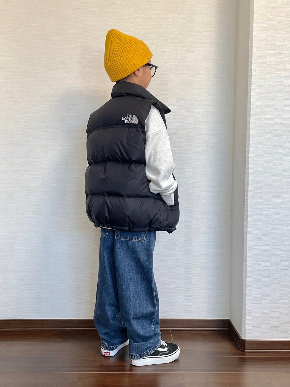 ブラック系のダウンベスト、ベージュ系のスウェット、ブルー系のデニムパンツを着用したキッズの冬コーディネートの2枚目の写真