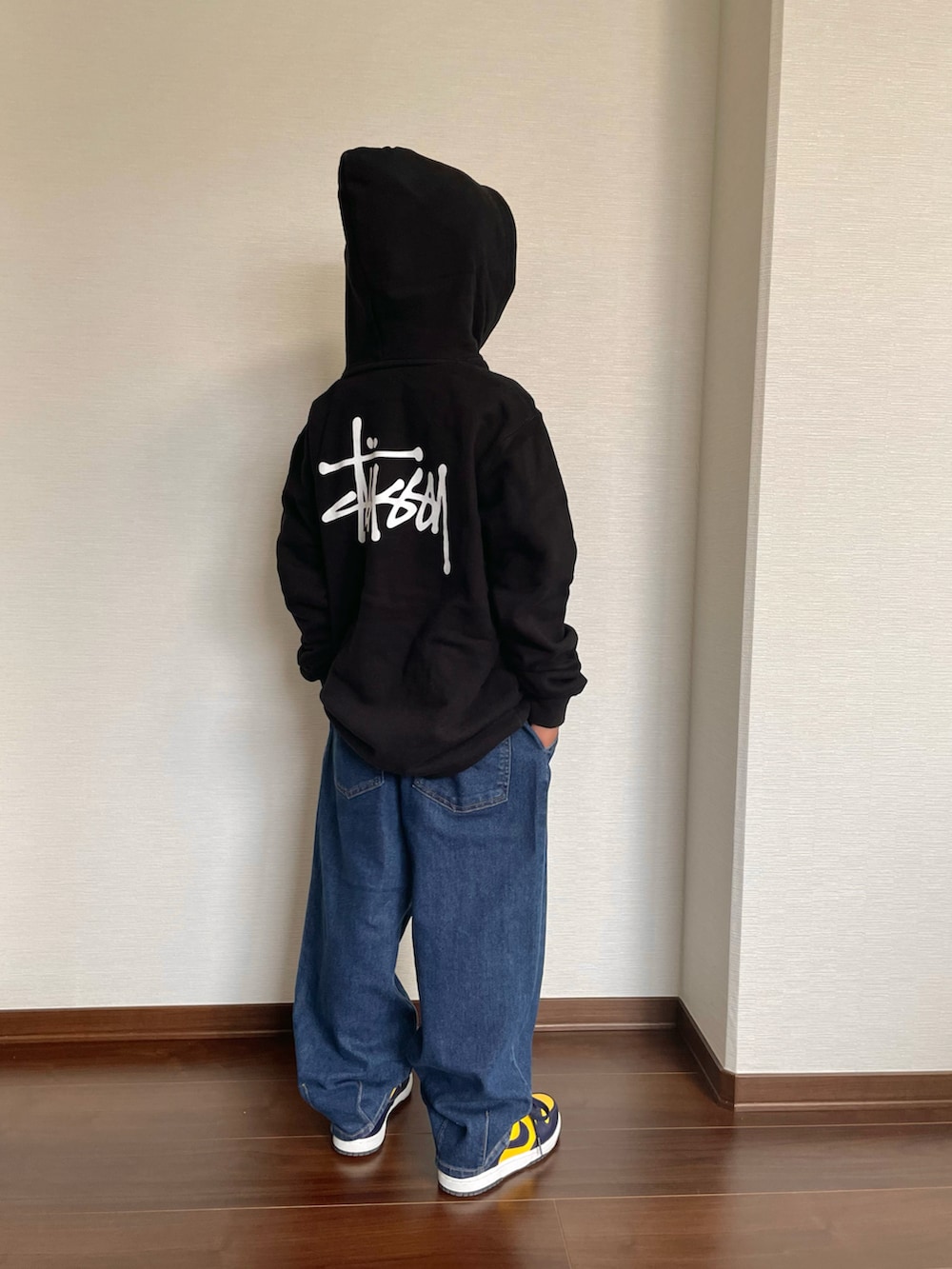ブラック系のパーカー、ブルー系のデニムパンツ、イエロー系のスニーカーを着用したキッズの秋コーディネートの2枚目の写真