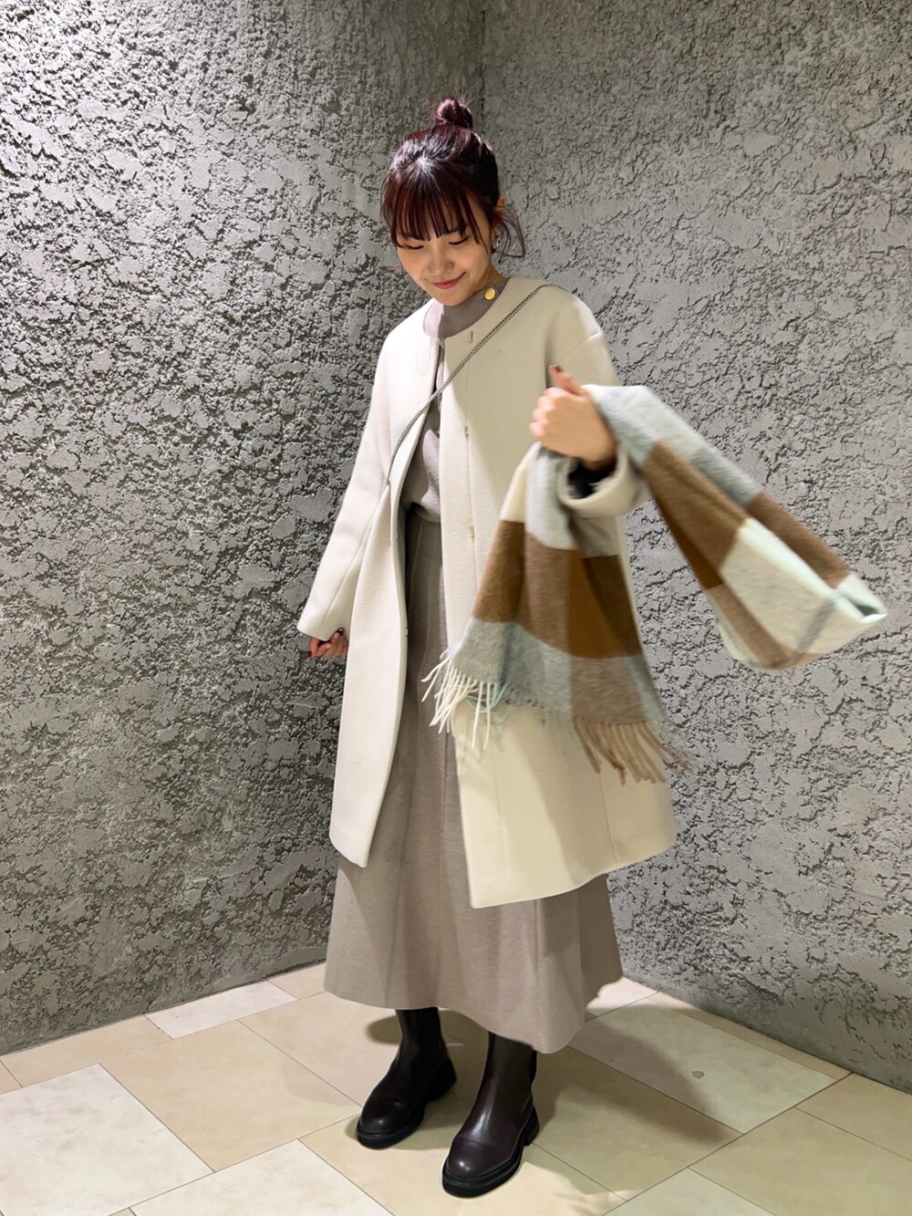 ベージュ系のノーカラーコート、ベージュ系のスカート、ブラウン系のブーツを着用したレディースの冬コーディネートの2枚目の写真
