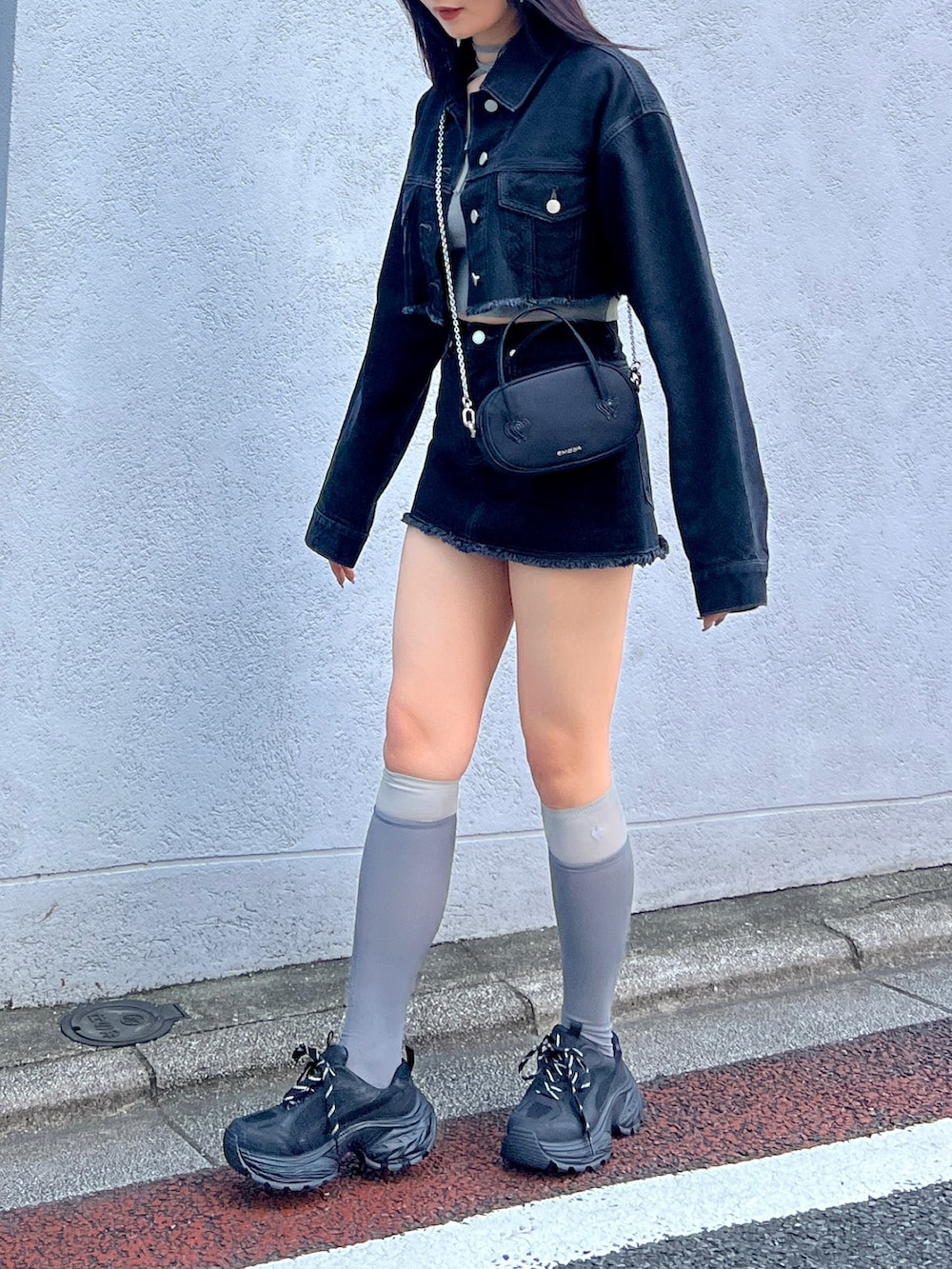 ブラック系のスカート、ブラック系のデニムジャケット、グレー系のニット/セーターを着用したレディースの夏コーディネートの3枚目の写真