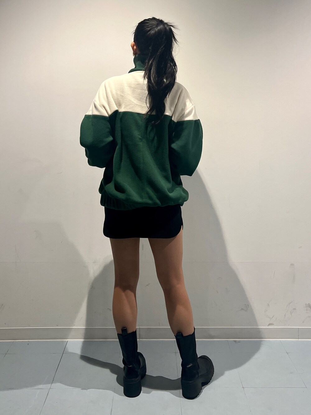 グリーン系のブルゾン、ブラック系のスカート、ブラック系のブーツを着用したレディースの秋コーディネートの3枚目の写真