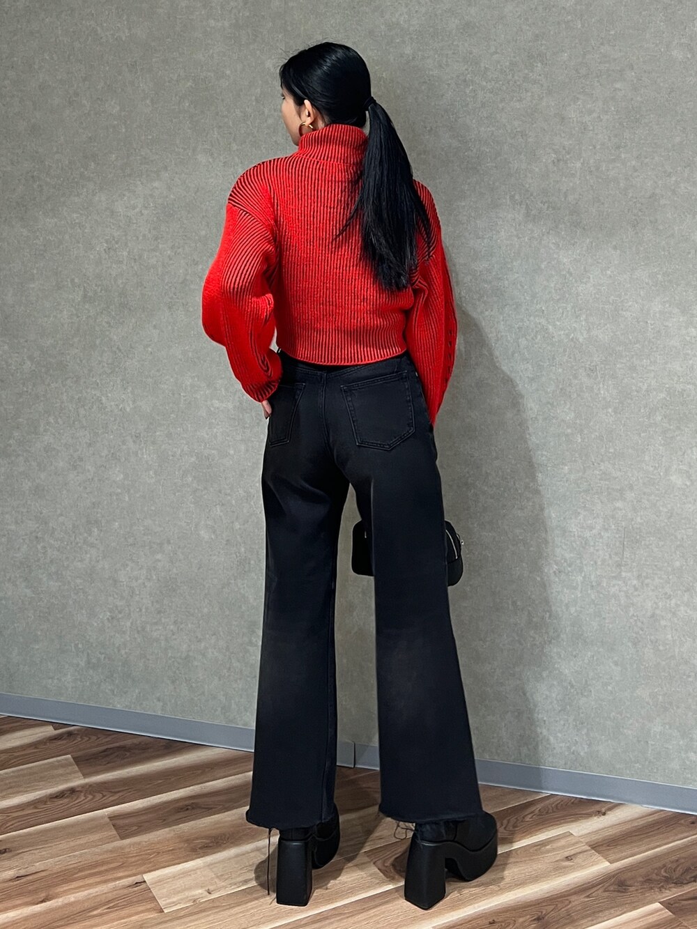 レッド系のニット/セーター、ブラック系のデニムパンツ、ブラック系のブーツを着用したレディースの秋コーディネートの5枚目の写真
