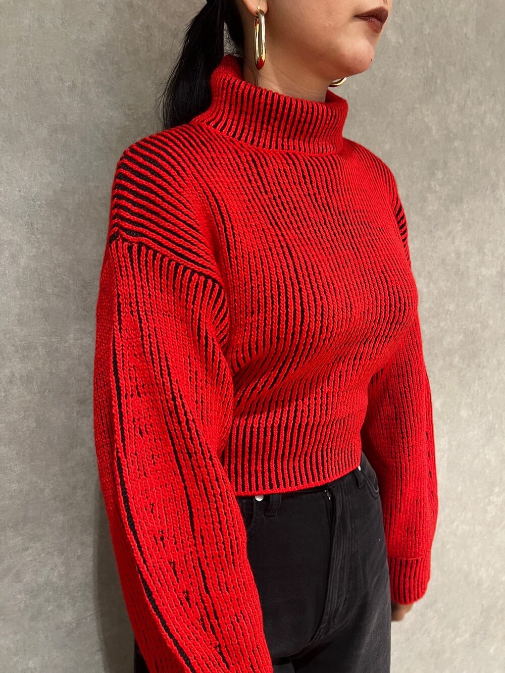 レッド系のニット/セーター、ブラック系のデニムパンツ、ブラック系のブーツを着用したレディースの秋コーディネートの6枚目の写真