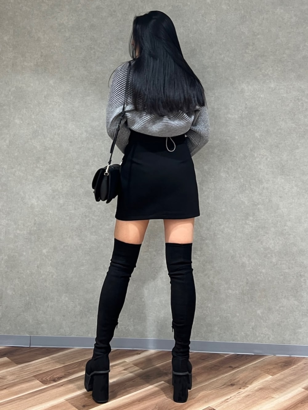 グレー系のニット/セーター、ブラック系のスカート、ブラック系のブーツを着用したレディースの秋コーディネートの2枚目の写真