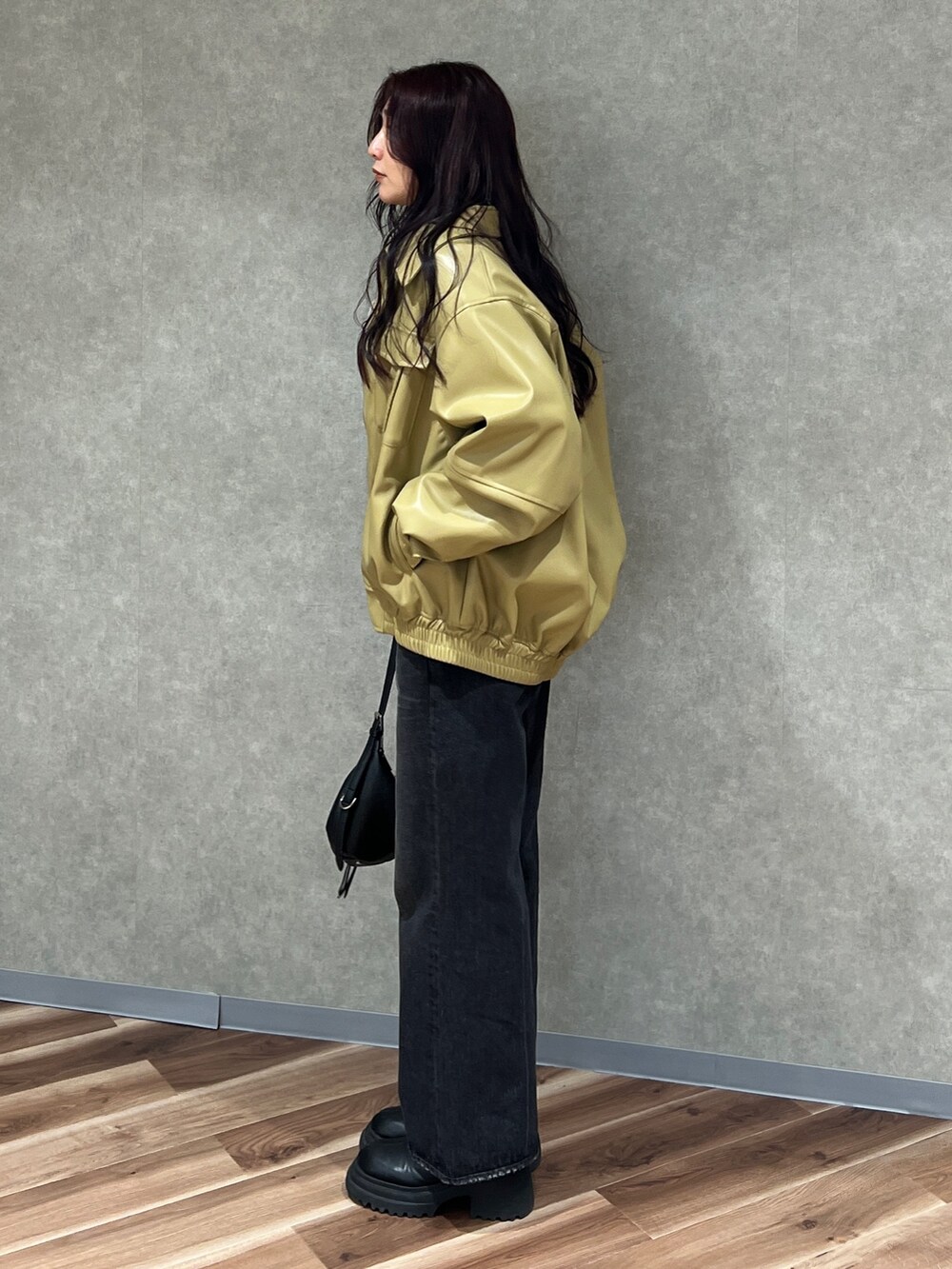 イエロー系のブルゾン、ブラック系のニット/セーター、ブラック系のデニムパンツを着用したレディースの冬コーディネートの2枚目の写真