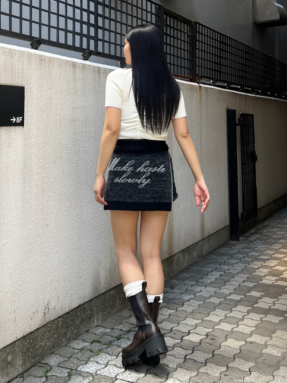 ホワイト系のニット/セーター、ブラック系のスカート、ブラウン系のブーツを着用したレディースの夏コーディネートの2枚目の写真