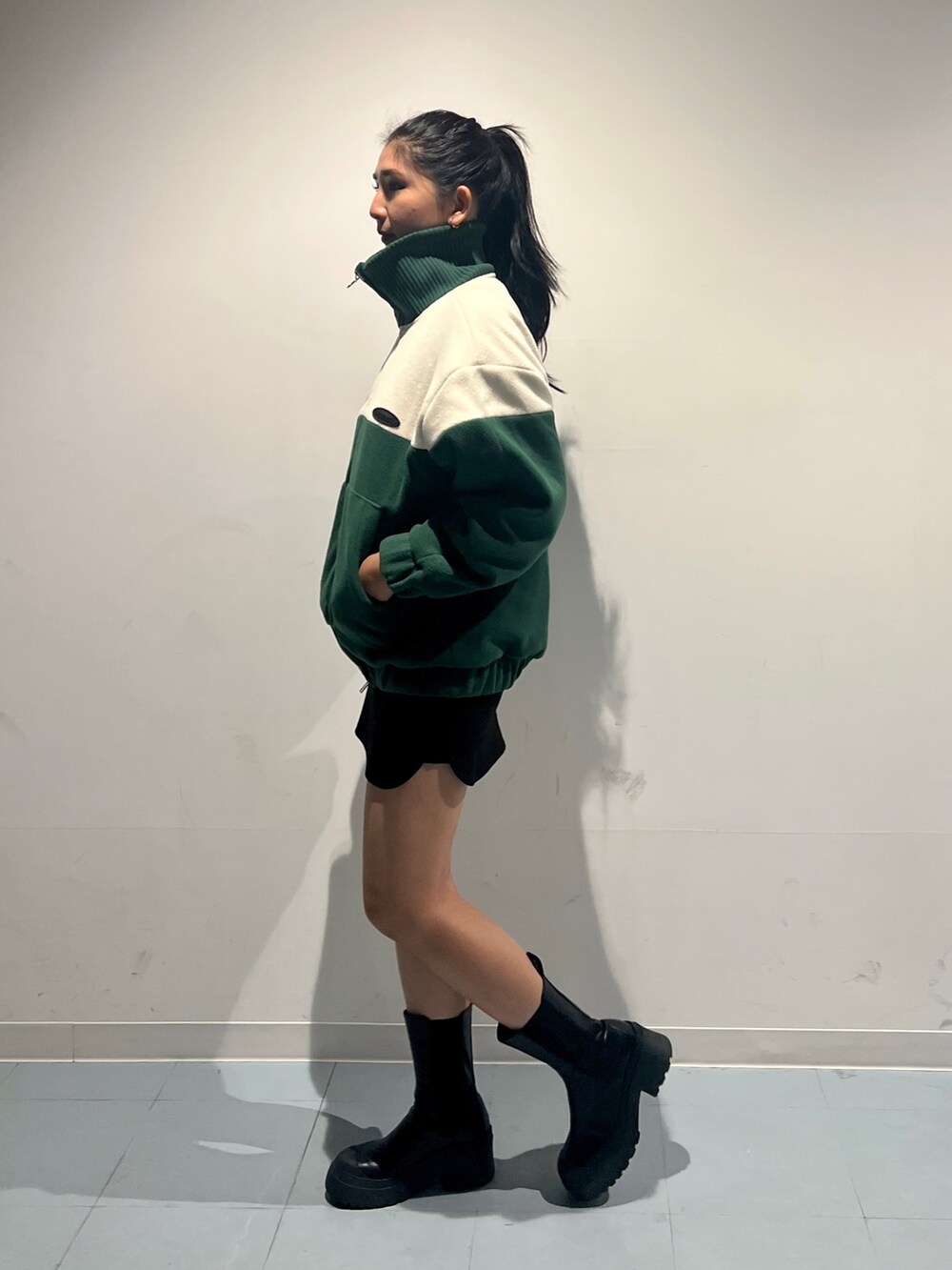 グリーン系のブルゾン、ブラック系のスカート、ブラック系のブーツを着用したレディースの秋コーディネートの2枚目の写真