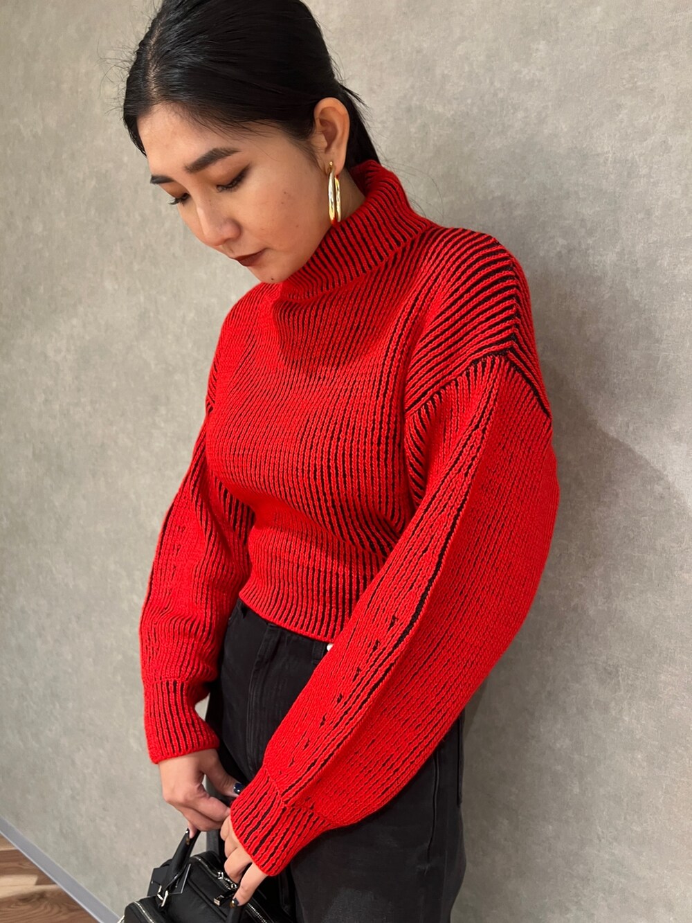 レッド系のニット/セーター、ブラック系のデニムパンツ、ブラック系のブーツを着用したレディースの秋コーディネートの7枚目の写真