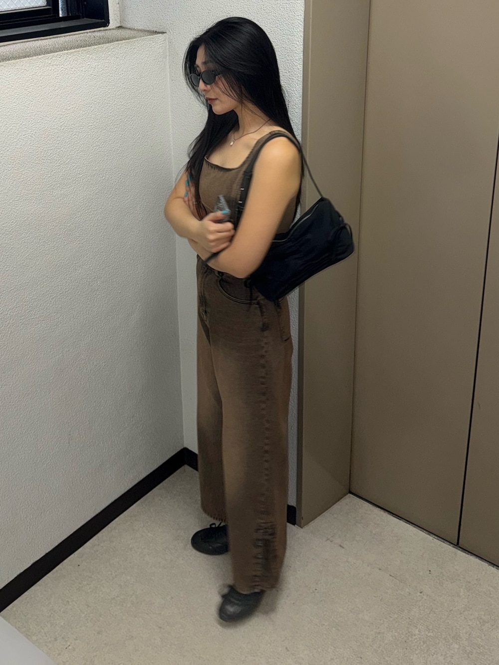 ブラウン系のデニムパンツ、ブラウン系のタンクトップ、ブラック系のスニーカーを着用したレディースの春コーディネートの2枚目の写真