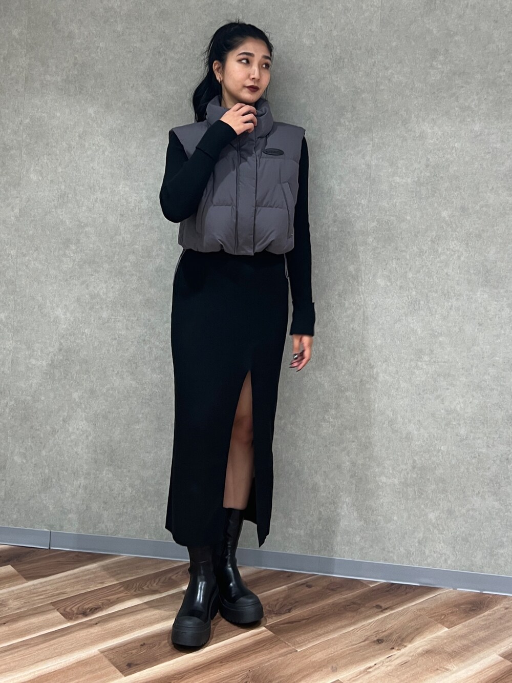 ブラック系のワンピース、グレー系のダウンベスト、ブラック系のブーツを着用したレディースの秋コーディネートの2枚目の写真