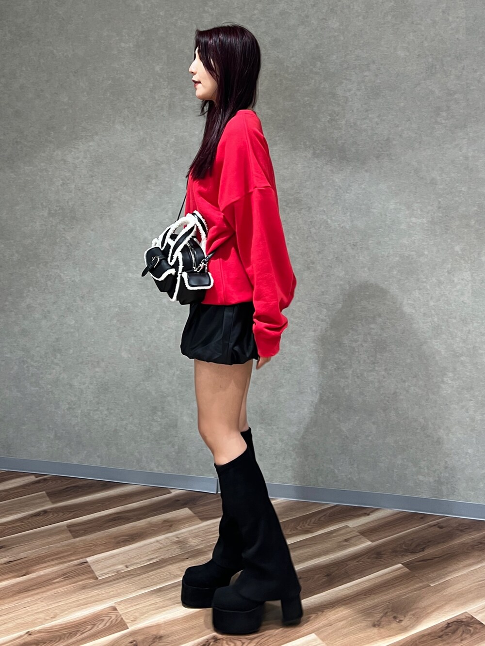レッド系のスウェット、ブラック系のハンドバッグ、ブラック系のブーツを着用したレディースの秋コーディネートの2枚目の写真