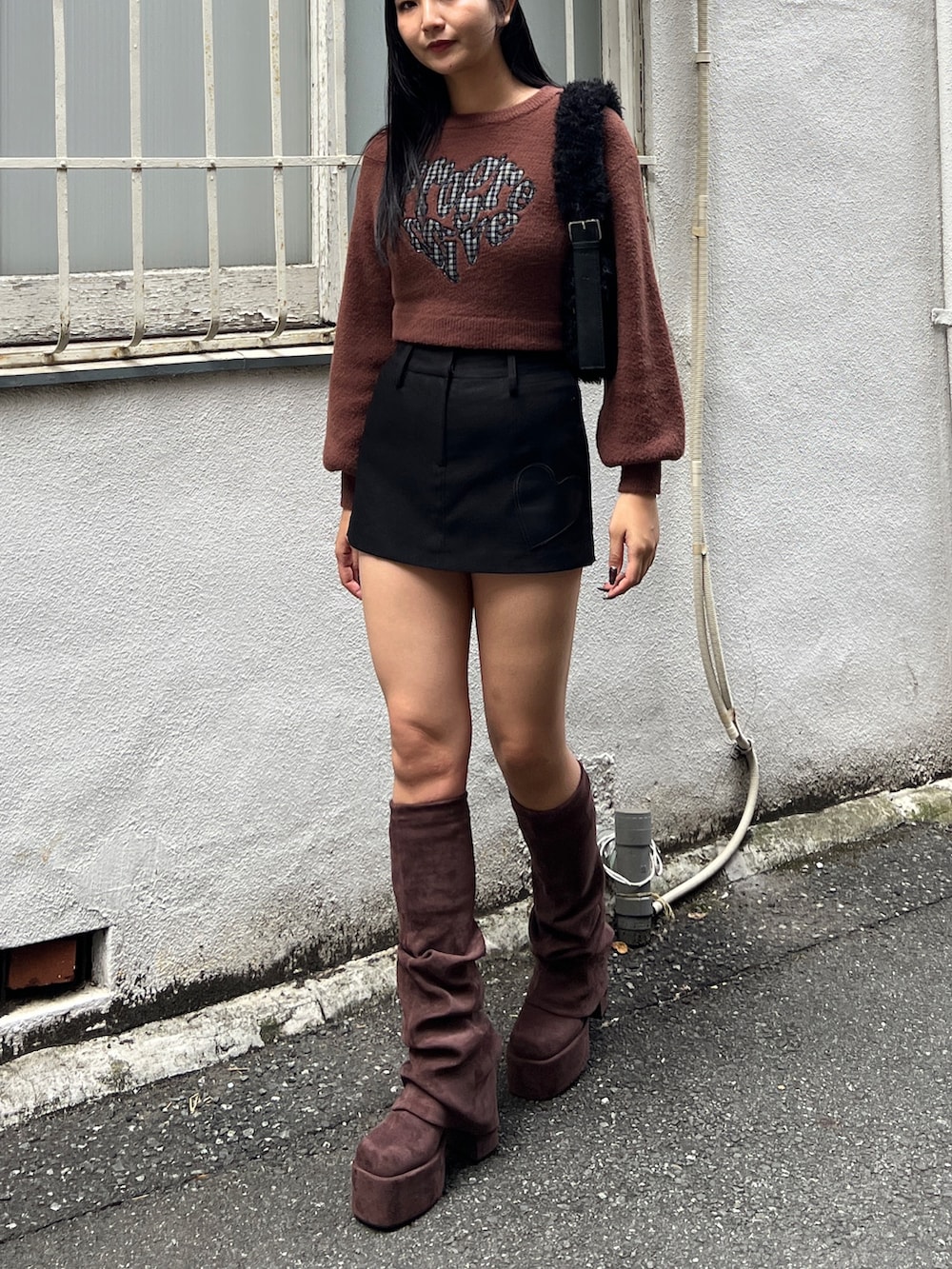 ブラウン系のニット/セーター、ブラック系のスカート、ブラウン系のブーツを着用したレディースの秋コーディネートの2枚目の写真