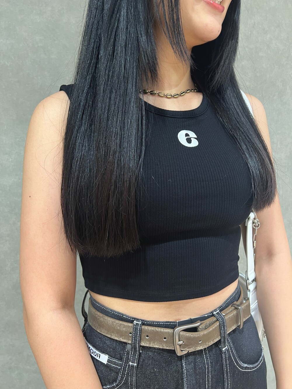 ブラック系のタンクトップ、ブルー系のデニムパンツ、ホワイト系のハンドバッグを着用したレディースの夏コーディネートの4枚目の写真