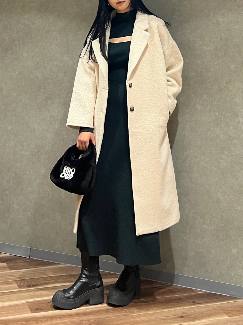 グリーン系のワンピース、ホワイト系のチェスターコート、ブラック系のハンドバッグを着用したレディースの冬コーディネートの2枚目の写真