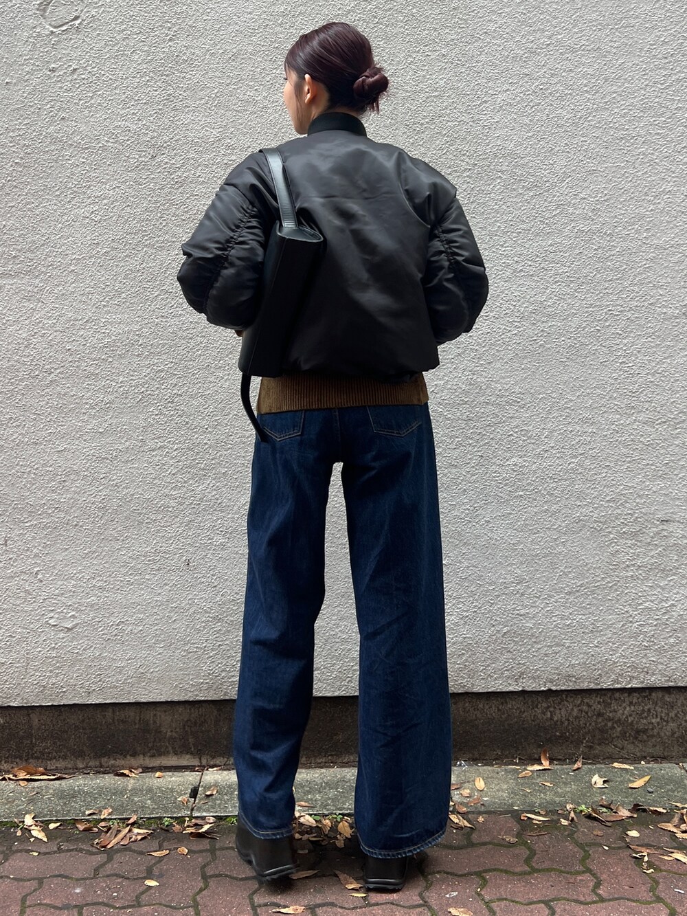ブラック系のブルゾン、ブルー系のデニムパンツ、ブラック系のハンドバッグを着用したレディースの秋コーディネートの3枚目の写真