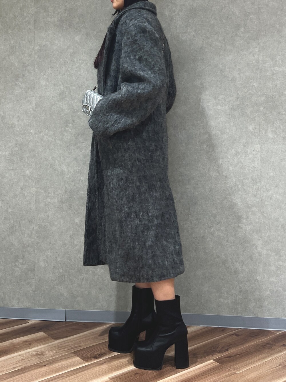 グレー系のチェスターコート、ブラック系のブーツ、ブラック系のニット/セーターを着用したレディースの冬コーディネートの2枚目の写真