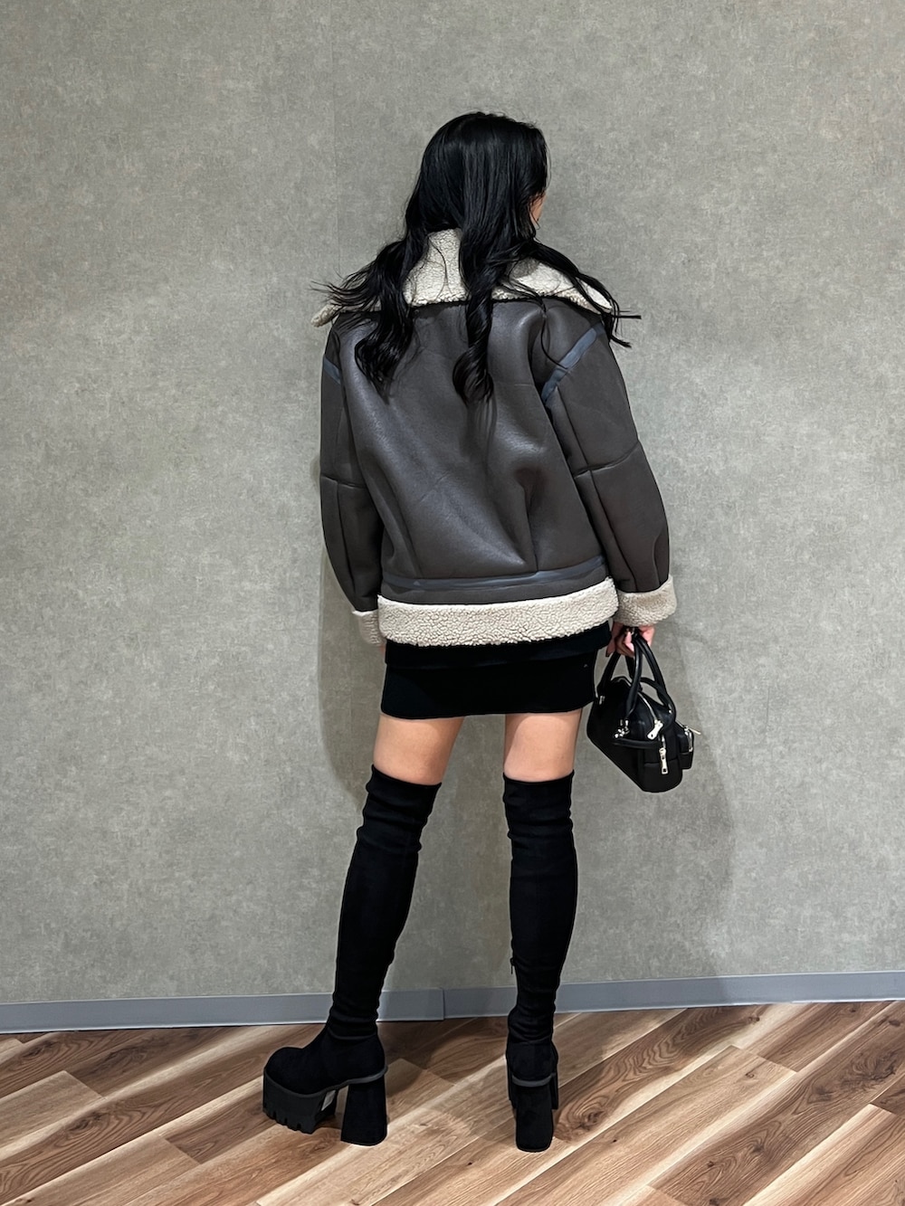 グレー系のムートンコート、ブラック系のカーディガン/ボレロ、ブラック系のスカートを着用したレディースの秋コーディネートの4枚目の写真