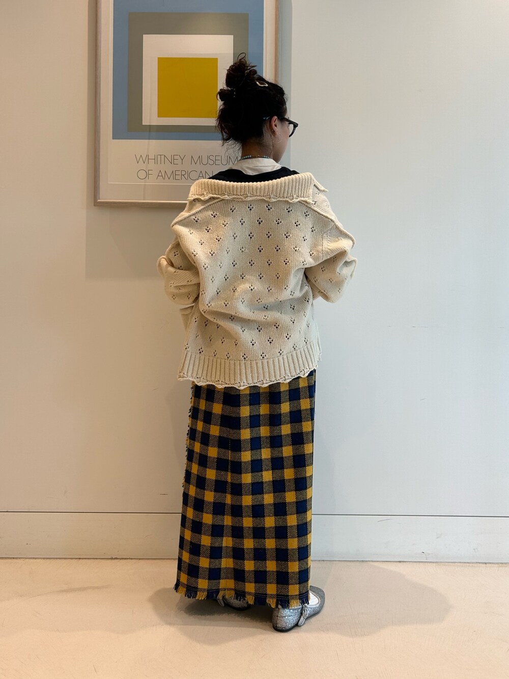 イエロー系のスカート、ホワイト系のカーディガン/ボレロ、ブラック系のメガネを着用したレディースの秋コーディネートの2枚目の写真