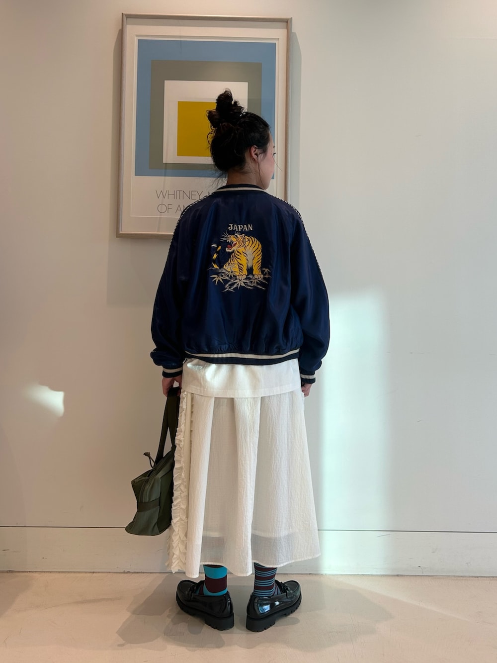 ブルー系のスカジャン、ホワイト系のスカート、ブラック系のローファーを着用したレディースの春コーディネートの2枚目の写真