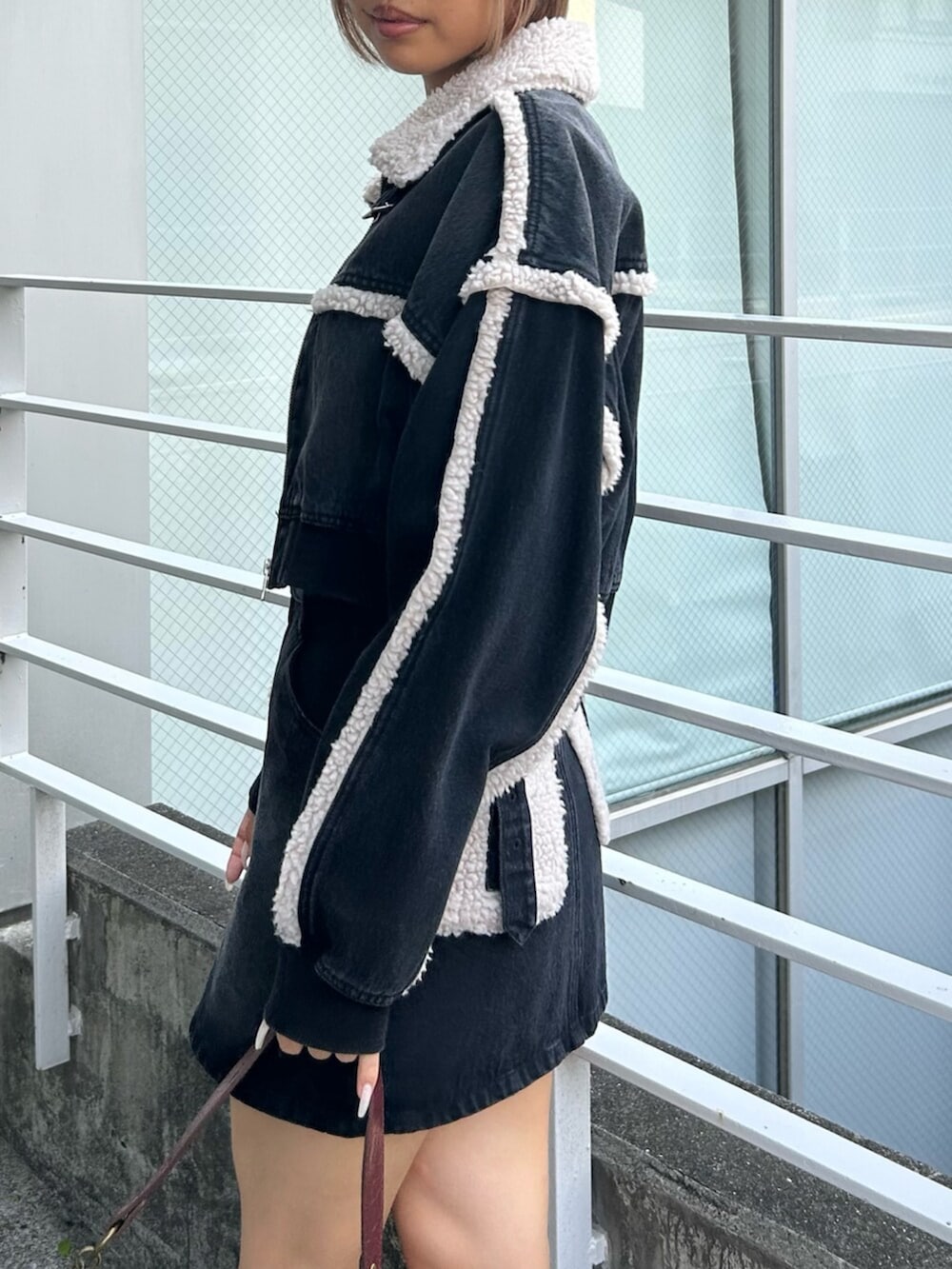 ブラック系のブルゾン、ブラック系のデニムスカート、ベージュ系のハンドバッグを着用したレディースの秋コーディネートの4枚目の写真