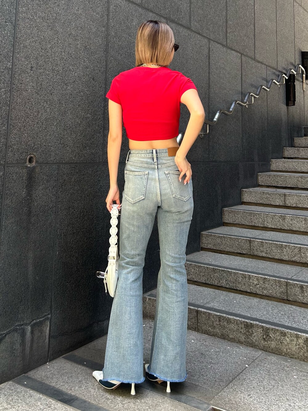 ブルー系のデニムパンツ、ホワイト系のパンプス、ホワイト系のショルダーバッグを着用したレディースの春コーディネートの2枚目の写真