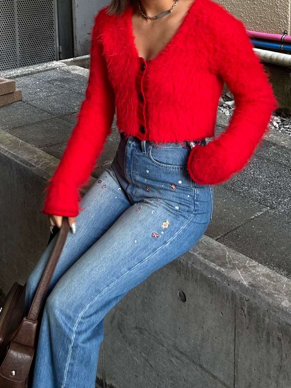 レッド系のニット/セーター、ブルー系のデニムパンツ、ブラウン系のハンドバッグを着用したレディースの夏コーディネートの2枚目の写真