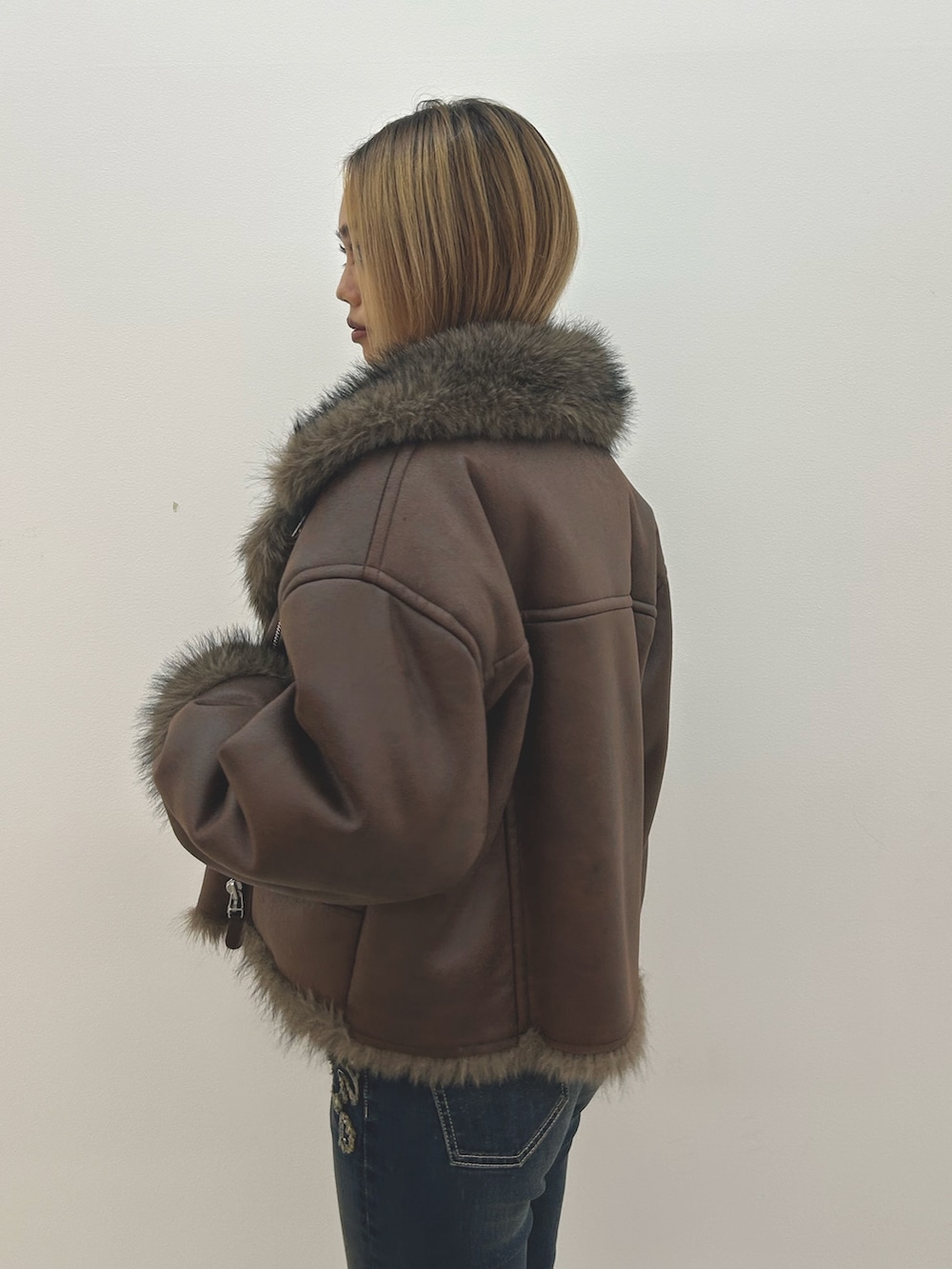 ブラウン系のブルゾン、ホワイト系のニット/セーター、ブルー系のデニムパンツを着用したレディースの秋コーディネートの5枚目の写真