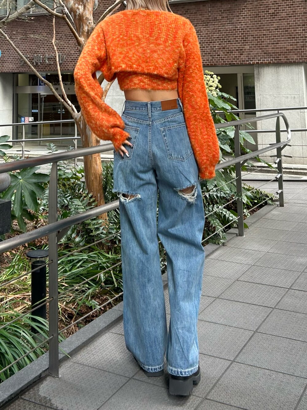 ブルー系のデニムパンツ、オレンジ系のニット/セーター、ブラック系のブーツを着用したレディースの冬コーディネートの2枚目の写真