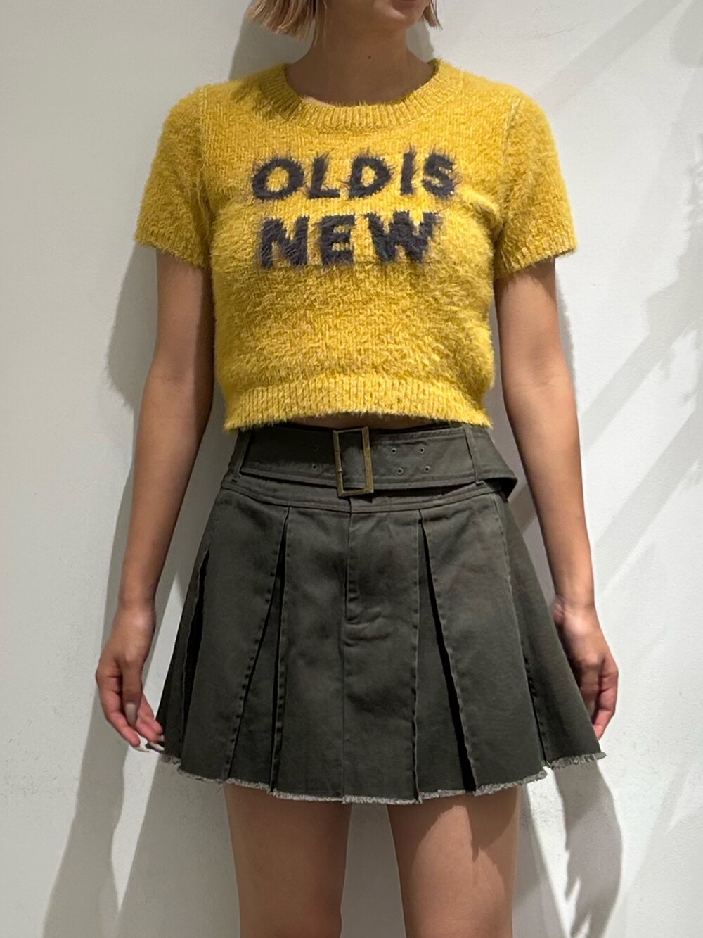 イエロー系のニット/セーター、グレー系のスカート、ブラック系のブーツを着用したレディースの夏コーディネートの2枚目の写真