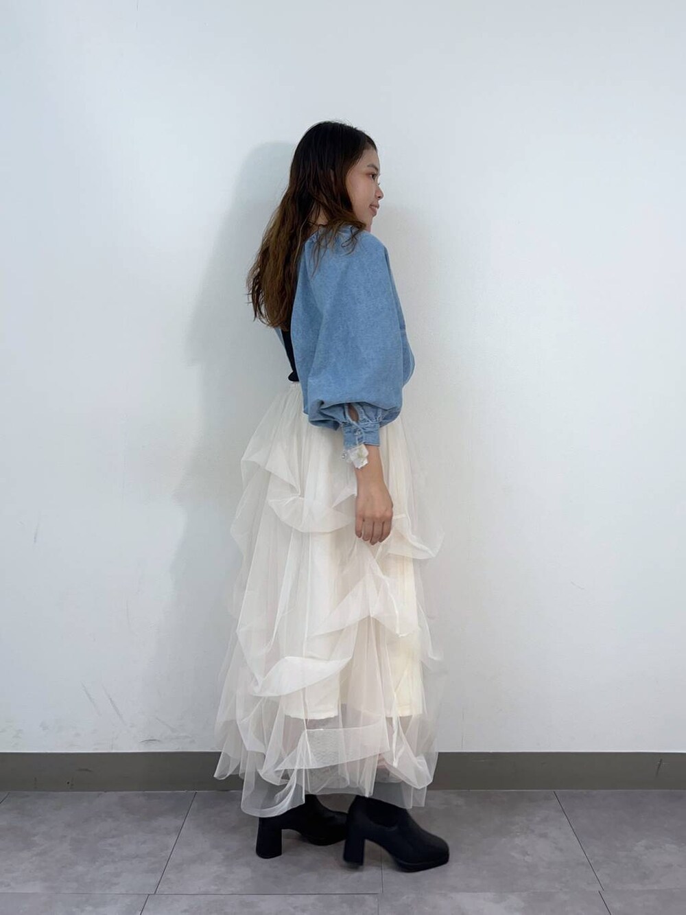 ブルー系のアンサンブル、ホワイト系のスカート、ブラック系のブーツを着用したレディースの秋コーディネートの2枚目の写真