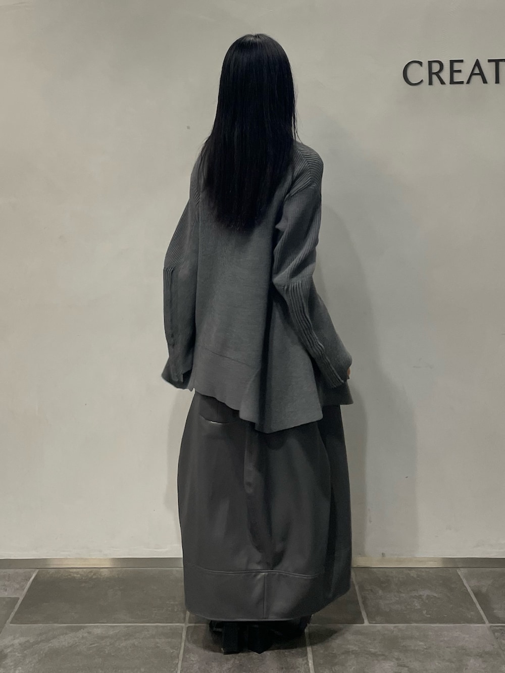 グレー系のニット/セーター、グレー系のスカート、ブラック系のブーツを着用したレディースの秋コーディネートの2枚目の写真