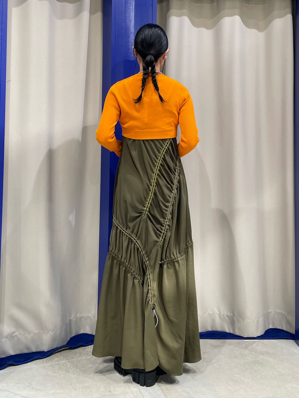 オレンジ系のニット/セーター、グリーン系のワンピース、ブラック系のサンダルを着用したレディースの春コーディネートの3枚目の写真