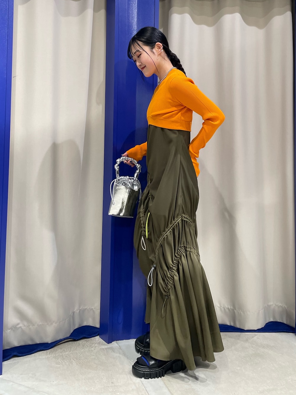 オレンジ系のニット/セーター、グリーン系のワンピース、ブラック系のサンダルを着用したレディースの春コーディネートの2枚目の写真