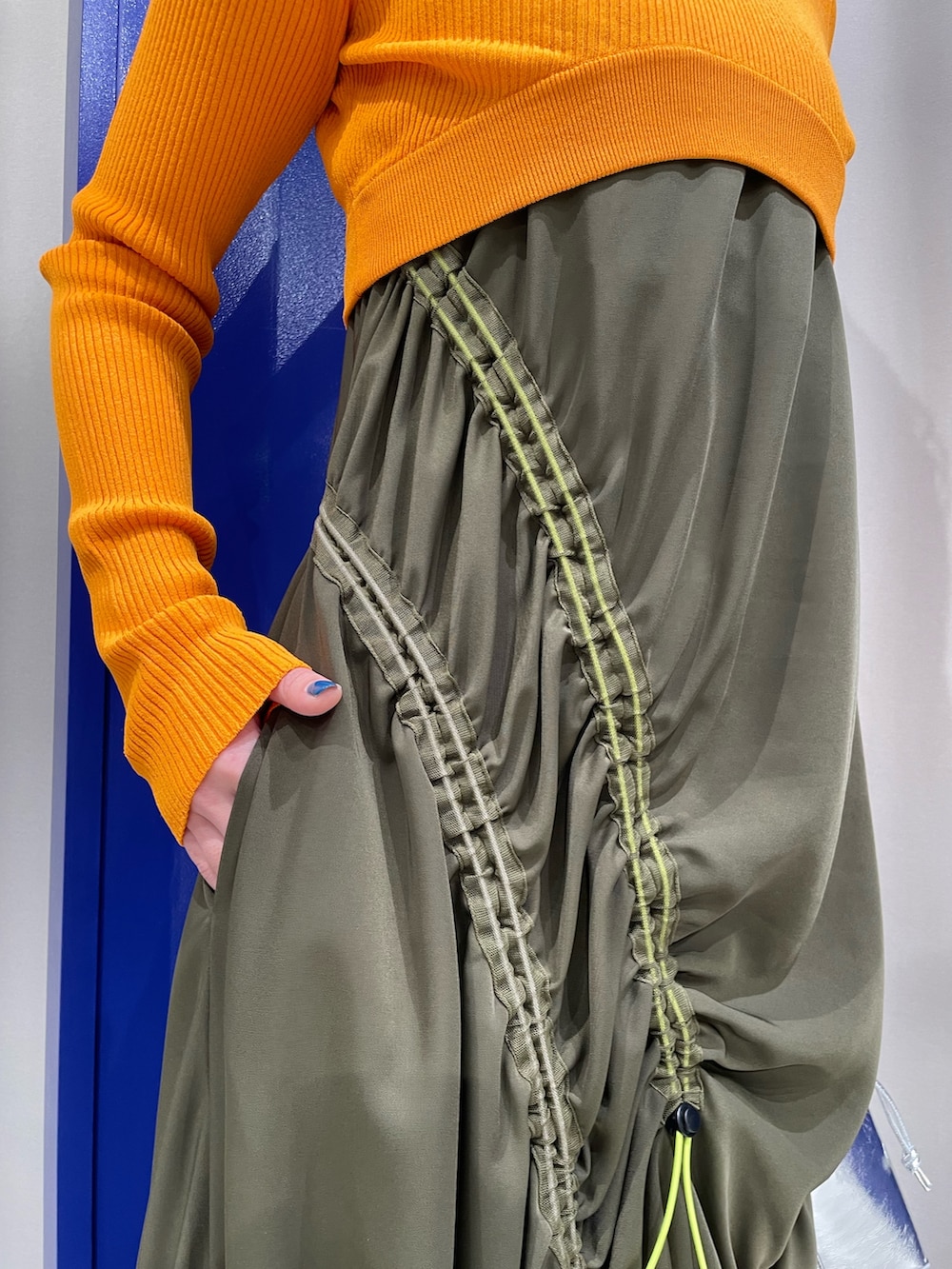 オレンジ系のニット/セーター、グリーン系のワンピース、ブラック系のサンダルを着用したレディースの春コーディネートの7枚目の写真