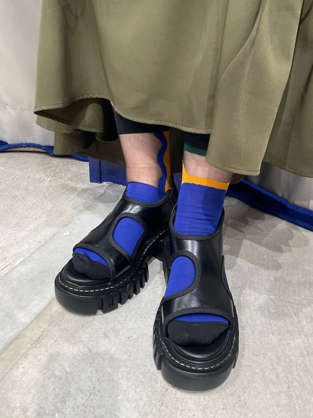 オレンジ系のニット/セーター、グリーン系のワンピース、ブラック系のサンダルを着用したレディースの春コーディネートの9枚目の写真