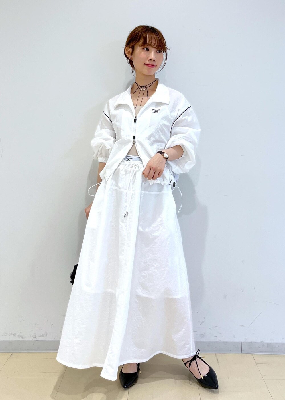 ブラック系のパンプス、ホワイト系のスカート、ベージュ系のキャミソールを着用したレディースの春コーディネートの2枚目の写真