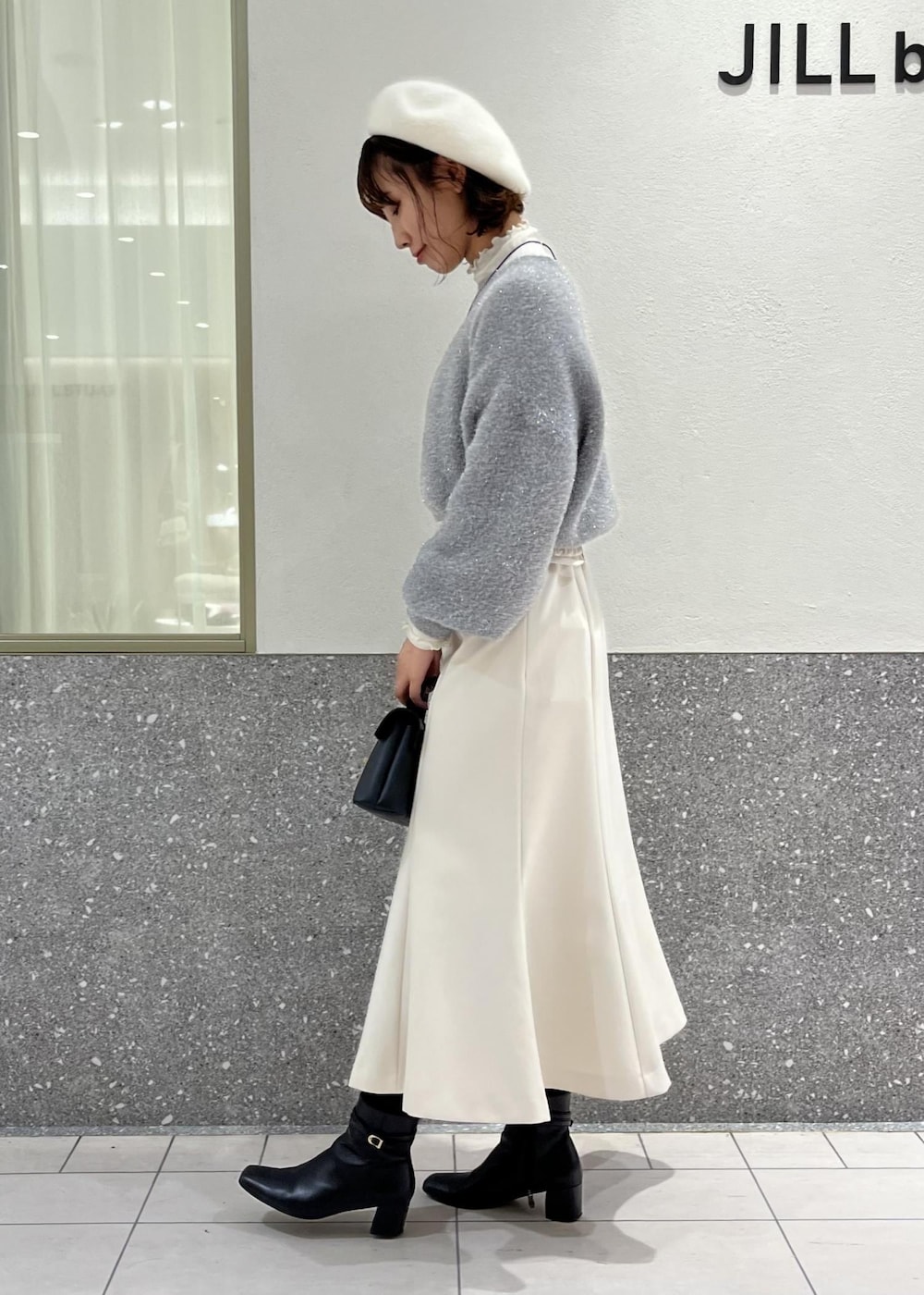 ホワイト系のTシャツ/カットソー、ホワイト系のスカート、グレー系のニット/セーターを着用したレディースの冬コーディネートの2枚目の写真